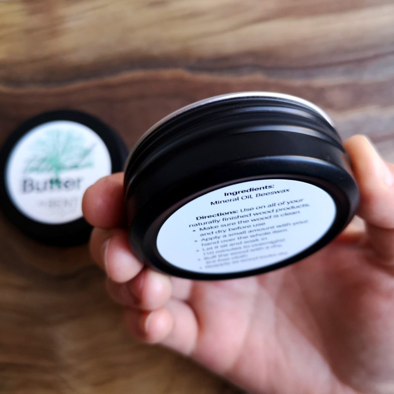 May include: A black metal tin with a white label that reads "Ingredients: Mineral Oil Beeswax" and "Directions: Use on all of your naturally finished wood products. Make sure the wood is clean and dry before use. Apply a small amount with your hand or a cloth and rub in with the grain. Let it dry and then buff with a clean cloth.  If needed, apply a second coat."