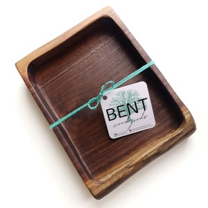 May include: A small, rectangular wooden tray with a natural wood finish. The tray is tied with a teal ribbon and a white tag that reads "BENT wood goods".