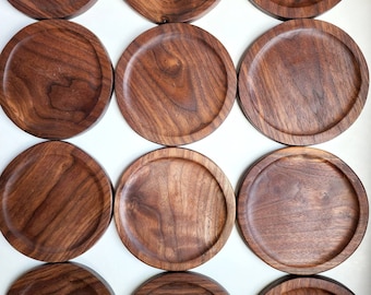 May include: Twelve round wooden coasters made of dark walnut wood. The coasters have a smooth, polished finish and are perfect for protecting surfaces from scratches and spills.