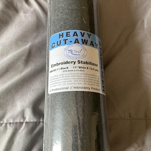 May include: A roll of black embroidery stabilizer, labeled "Heavy Cut-Away." The label indicates it is 11 inches wide and 12.5 yards long, designed for professional and home embroidery use.