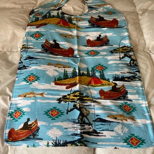 May include: A blue and white fabric with a repeating pattern of canoes, fishermen, and fish. The fabric has a red, green, and yellow geometric pattern in the background.
