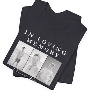 May include: Black t-shirt with the text "IN LOVING MEMORY" above three black and white photos. The name "David" is printed below the photos in cursive. The t-shirt is folded.