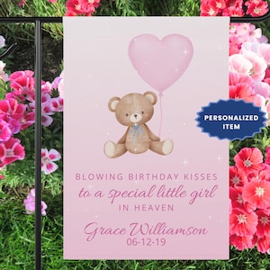 May include: A rectangular pink garden flag featuring a brown teddy bear holding a pink heart-shaped balloon. The text reads: BLOWING BIRTHDAY KISSES to a special little girl IN HEAVEN, Grace Williamson, 06-12-19. A blue badge states: PERSONALIZED ITEM.