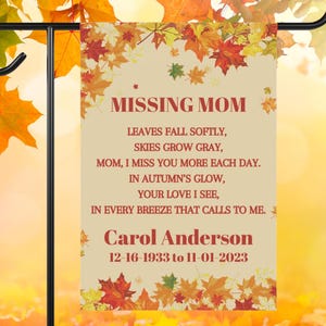May include: A garden flag with the text "MISSING MOM" in burgundy. The flag includes a poem about missing a mother and the name "Carol Anderson" with dates 12-16-1933 to 11-01-2023. The flag has a beige background with autumn leaves.