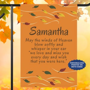 May include: A rectangular orange garden flag featuring a pattern of scattered autumn leaves in yellow, green, and dark red. The text reads: Samantha, May the winds of Heaven blow softly and whisper in your ear we love and miss you every day.