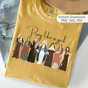 May include: Mustard yellow t-shirt with the phrase "Pray like a girl" in black script. The shirt features an illustration of several women in religious attire. The words "Instant Download PNG SVG PDF" are also visible.