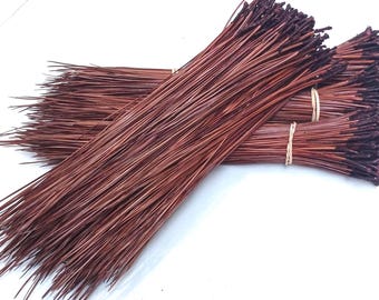 May include: Bundles of long, reddish-brown pine needles, tightly bound with rubber bands. The needles have a natural, textured appearance, with darker tips. The bundles are arranged on a white surface, creating a rustic, natural aesthetic.