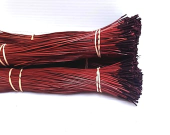 May include: Bundles of red-brown incense sticks, tightly bound with cream-colored rubber bands. The tips of the incense are a darker shade of brown. The sticks are arranged in a layered pattern against a white background.