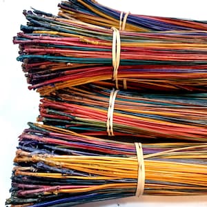 May include: Bundles of colorful, dyed pine needles, tightly bound with tan rubber bands. The needles display a vibrant spectrum of colors, including red, yellow, blue, and green. The ends of the needles have a darker, textured appearance.