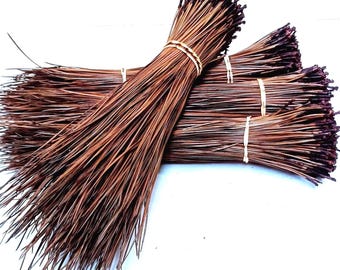 May include: A collection of dried, brown pine needles bundled together with thin, light-colored twine. The needles are long, slender, and pointed, arranged in several overlapping clusters that create a textured, fan-like appearance.