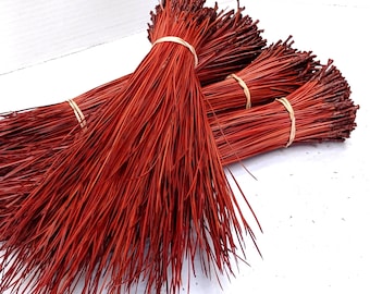 May include: A bundle of red dyed pine needles, tied together with rubber bands. The needles are long and thin, and they are arranged in a fan shape.