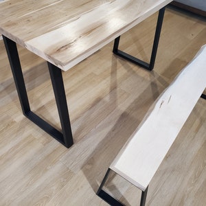 May include: A wooden table with a live edge top and black metal legs. Two matching benches with live edge tops and black metal legs are placed in front of the table.