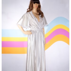 May include: A long, silver-colored robe with short sleeves and a V-neckline. The robe features a cinched waist and delicate lace trim along the neckline and sleeve edges. The garment is displayed on a mannequin.