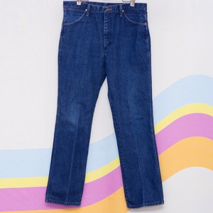 May include: Dark blue denim jeans with a classic five-pocket design. The jeans have a straight leg cut and are hanging on a hanger. The denim has a slight fade in the front. The jeans are a medium wash.