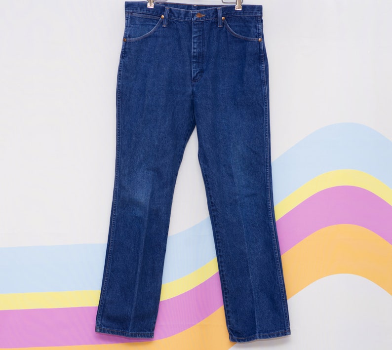 May include: Dark blue denim jeans with a classic five-pocket design. The jeans have a straight leg cut and are hanging on a hanger. The denim has a slight fade in the front. The jeans are a medium wash.