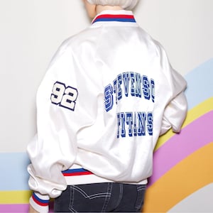May include: White satin bomber jacket with blue and red trim. The jacket features the number "92" on the left sleeve and the words "STEVENSON TITANS" in blue lettering on the back. The jacket is a classic athletic style.