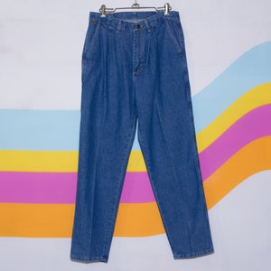 Puede incluir: Pantalones vaqueros azules con la parte delantera plisada, colgados de una percha met&aacute;lica. Los pantalones tienen un corte cl&aacute;sico de pierna recta y cuentan con bolsillos y cierre de bot&oacute;n. El fondo tiene un dise&ntilde;o de rayas de arco&iacute;ris colorido.