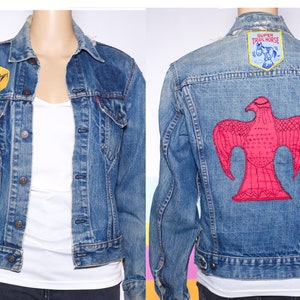 May include: Vintage blue denim jacket with patches. Features a horse patch on the front and a red bird design on the back. The jacket has a classic button-up design with front pockets and a collared neckline.