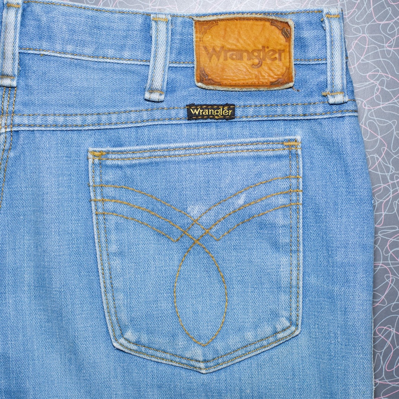 Puede incluir: Vaqueros de mezclilla azul claro con un parche de cuero Wrangler y una peque&ntilde;a etiqueta Wrangler. El bolsillo trasero presenta un dise&ntilde;o de costura decorativo. Vaqueros de estilo cl&aacute;sico.