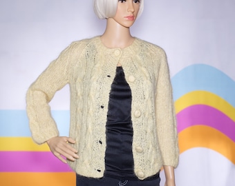 May include: A light yellow, vintage-style cardigan sweater with a round neckline and three-quarter sleeves. The sweater features a cable knit design on the front panels and is fastened with large, round buttons. The garment is displayed on a mannequin.