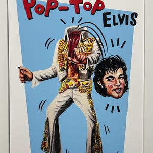 May include: A framed art print titled Pop-Top Elvis featuring a headless figure in a white jumpsuit with gold embellishments, with a detached head floating to the right. The background is light blue, and the artist signature is in the bottom right.