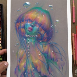 Pode incluir: Uma impressão artística de 23 cm por 30 cm em papel cinzento com uma ilustração colorida de uma figura com cabelo e pele iridescentes, adornada com pérolas e rodeada por bolhas flutuantes, ao lado de um conjunto de pastéis e lápis de cor.