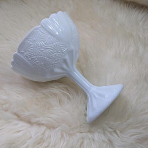 Puede incluir: Un cuenco blanco para postre, con pie, borde festoneado y un patrón texturizado detallado. El tallo y la base también son blancos, creando un diseño elegante y cohesivo. Este cuenco de estilo vintage es perfecto para servir postres.