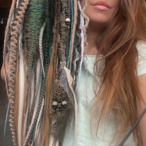 May include: A set of synthetic dreadlocks in various shades of brown, white, and green. The dreadlocks are decorated with beads and a lace trim.