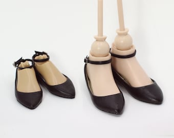 May include: Four black ankle strap doll shoes with pointed toes. The shoes are on a white background.