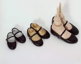 May include: Four pairs of black leather doll shoes with a strap and buckle. The shoes are on a white background.