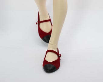 May include: A pair of red suede doll shoes with black patent leather toes and a buckle strap.