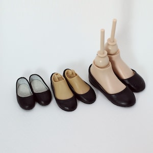 May include: Five pairs of black doll shoes in various sizes. The shoes are all flat and have a simple design.