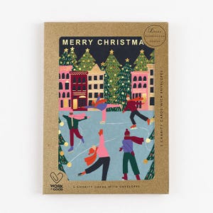 Könnte beinhalten: Ein Set Weihnachtskarten in einer braunen Pappschachtel. Die Karten zeigen eine Illustration von Menschen, die vor Gebäuden und Weihnachtsbäumen Schlittschuh laufen. Der Text "MERRY CHRISTMAS" steht oben.