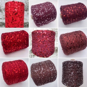 Può includere: Nove bobine di filo rosso e bordeaux con paillettes. Il filo è avvolto attorno alle bobine e le paillettes sono sparse nel filo.