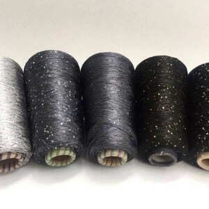 Könnte beinhalten: Fünf Garnrollen mit Glitter in Silber, Schwarz und zwei Schattierungen von Dunkelgrau.