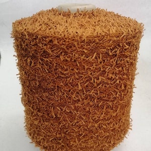 May include: A spool of brown yarn with a fuzzy texture. The yarn is tightly wound and has a rough, uneven surface.
