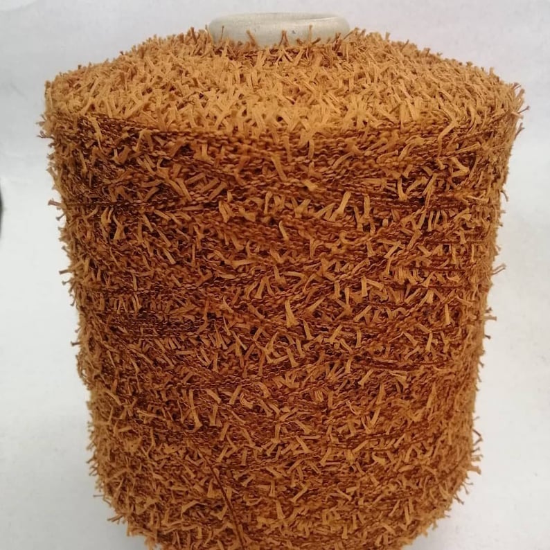 May include: A spool of brown yarn with a fuzzy texture. The yarn is tightly wound and has a rough, uneven surface.