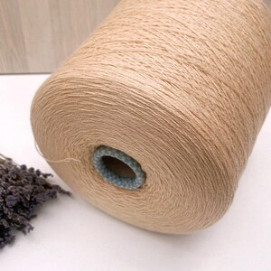 May include: A beige skein of yarn wound on a cardboard spool with a blue and white patterned center.