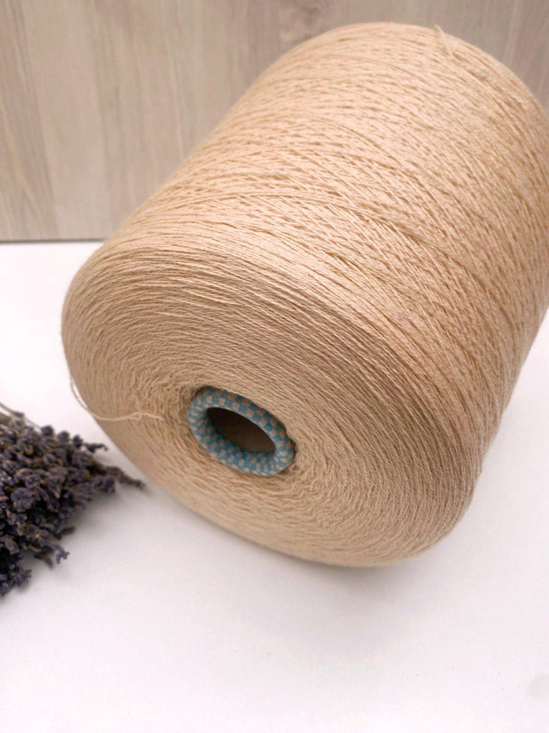 May include: A beige skein of yarn wound on a cardboard spool with a blue and white patterned center.