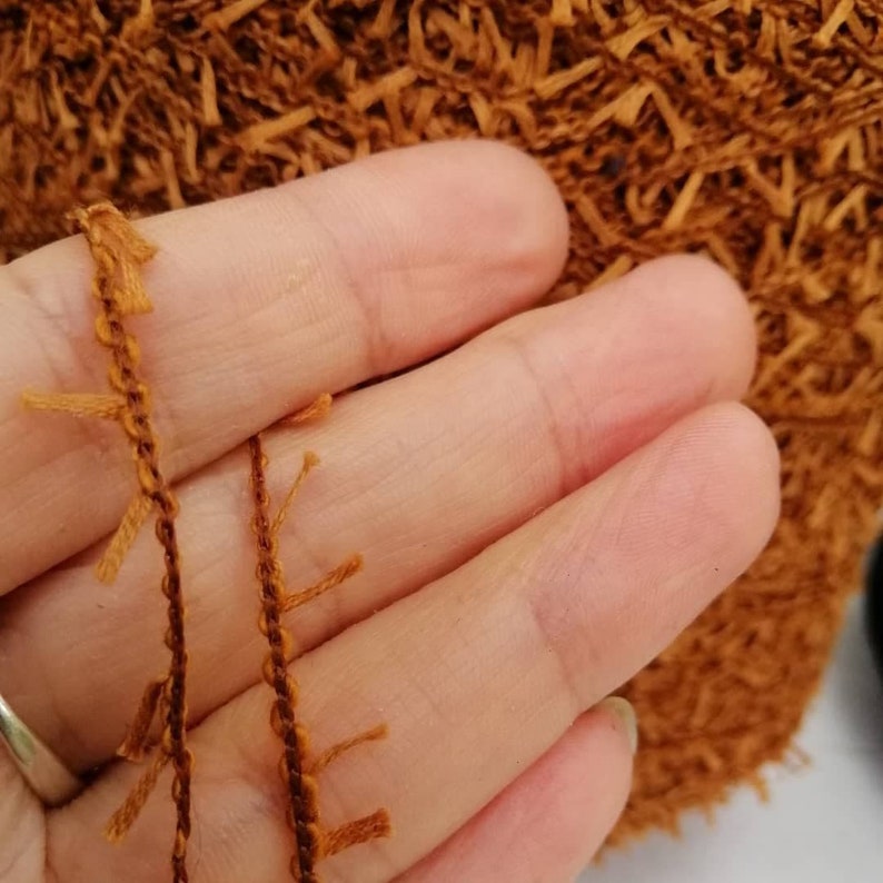 May include: Close-up of a brown yarn with fringe. The yarn is held in a hand.