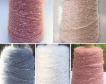 May include: Four spools of yarn in different colors: pink, white, blue, and a darker pink. Each spool has a fuzzy texture and is decorated with small, shiny beads.