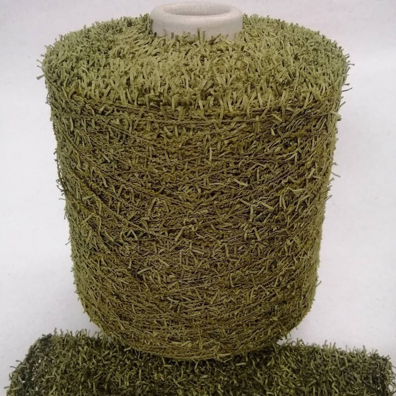 May include: A spool of green yarn with a fuzzy texture. The yarn is wound around a cardboard tube.