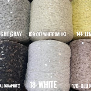 May include: Six spools of yarn with sequins, in the colors light gray, off white, lemon, charcoal, white, and old rose. The spools are labeled with their color and number.
