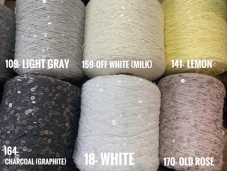 May include: Six spools of yarn with sequins, in the colors light gray, off white, lemon, charcoal, white, and old rose. The spools are labeled with their color and number.