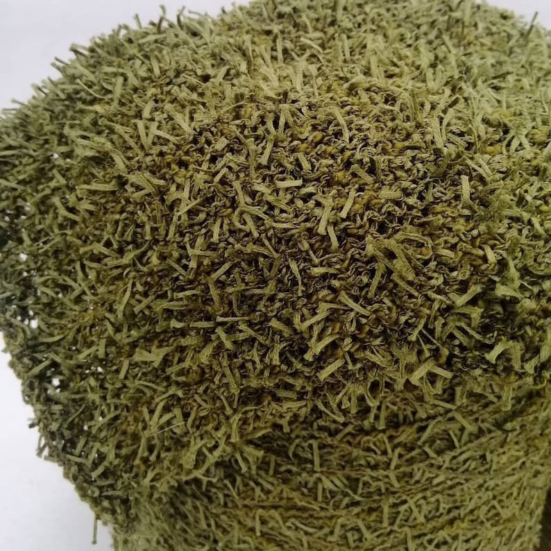 May include: Close-up of a green, textured fabric with a fuzzy, frayed surface. The fabric has a woven appearance and is made of thin, shredded strands.