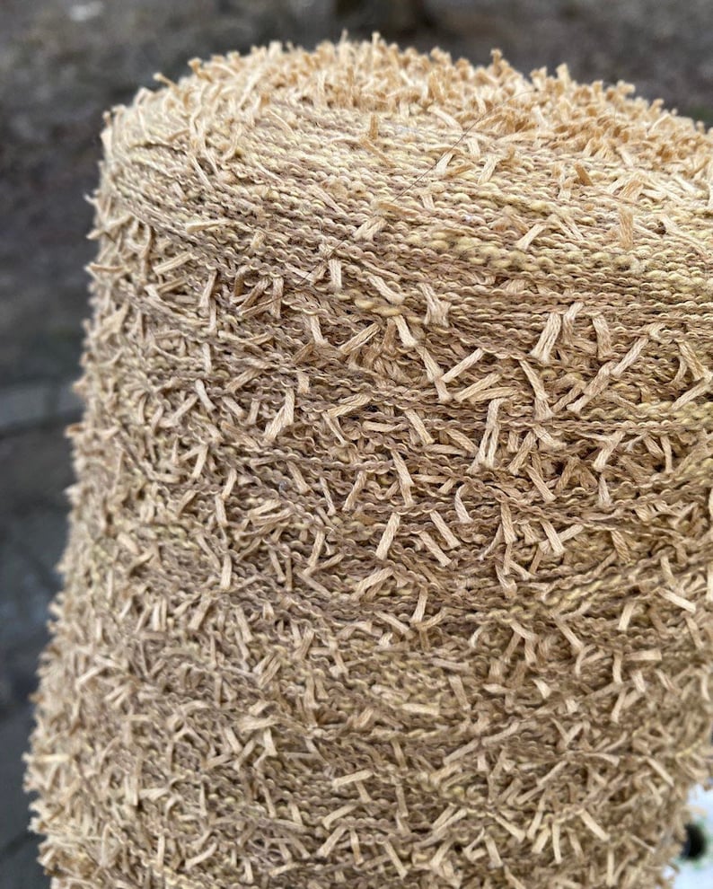 May include: A close-up of a skein of beige yarn with a fuzzy texture. The yarn is tightly wound and has a subtle sheen.