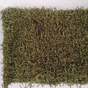 May include: A close-up of a green, shaggy rug made of shredded fabric. The rug has a textured, fuzzy surface and is perfect for adding a touch of rustic charm to any room.
