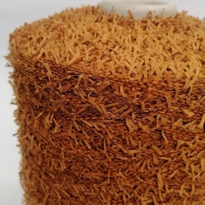 May include: Close-up of a spool of brown yarn with a fuzzy texture. The yarn is made of thin strands that are twisted together to create a soft, fluffy look.