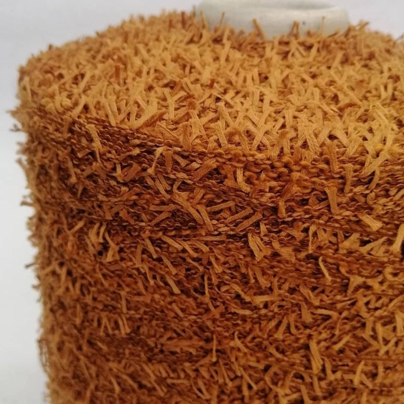 May include: Close-up of a spool of brown yarn with a fuzzy texture. The yarn is made of thin strands that are twisted together to create a soft, fluffy look.