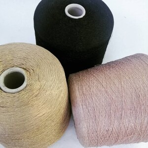 May include: Three spools of yarn in different colors: black, gold, and pink. The spools are made of a soft, textured material.